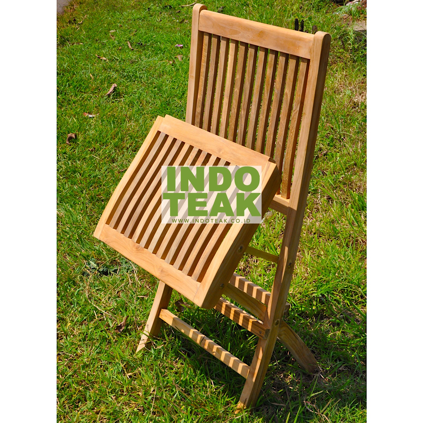 Premium solid teak folding chair on green grass field by Indoteak Indonesia, luxury teak outdoor garden furniture manufacturer