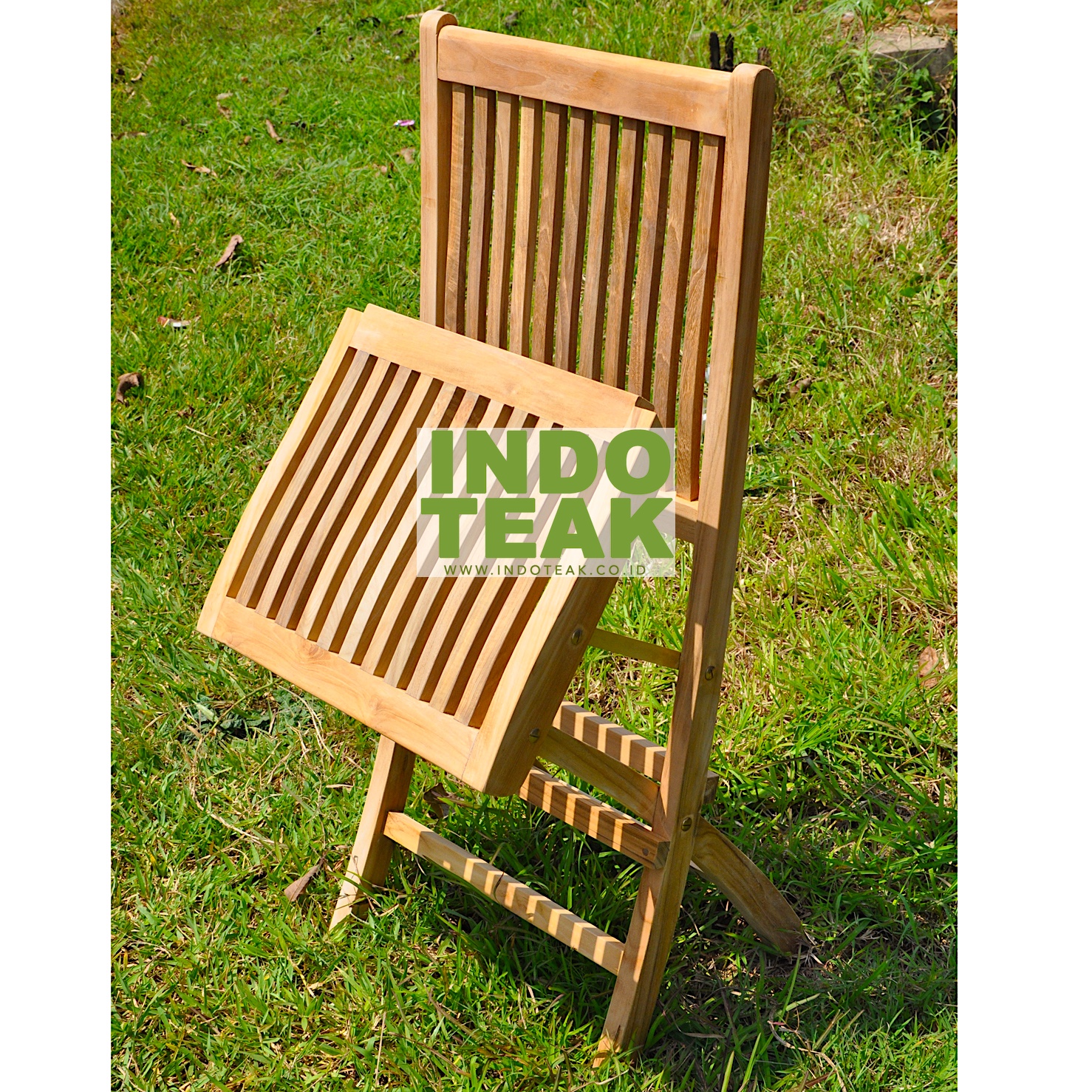 Premium solid teak folding arm chair on green grass field by Indoteak Indonesia, luxury teak outdoor garden furniture manufacturer
