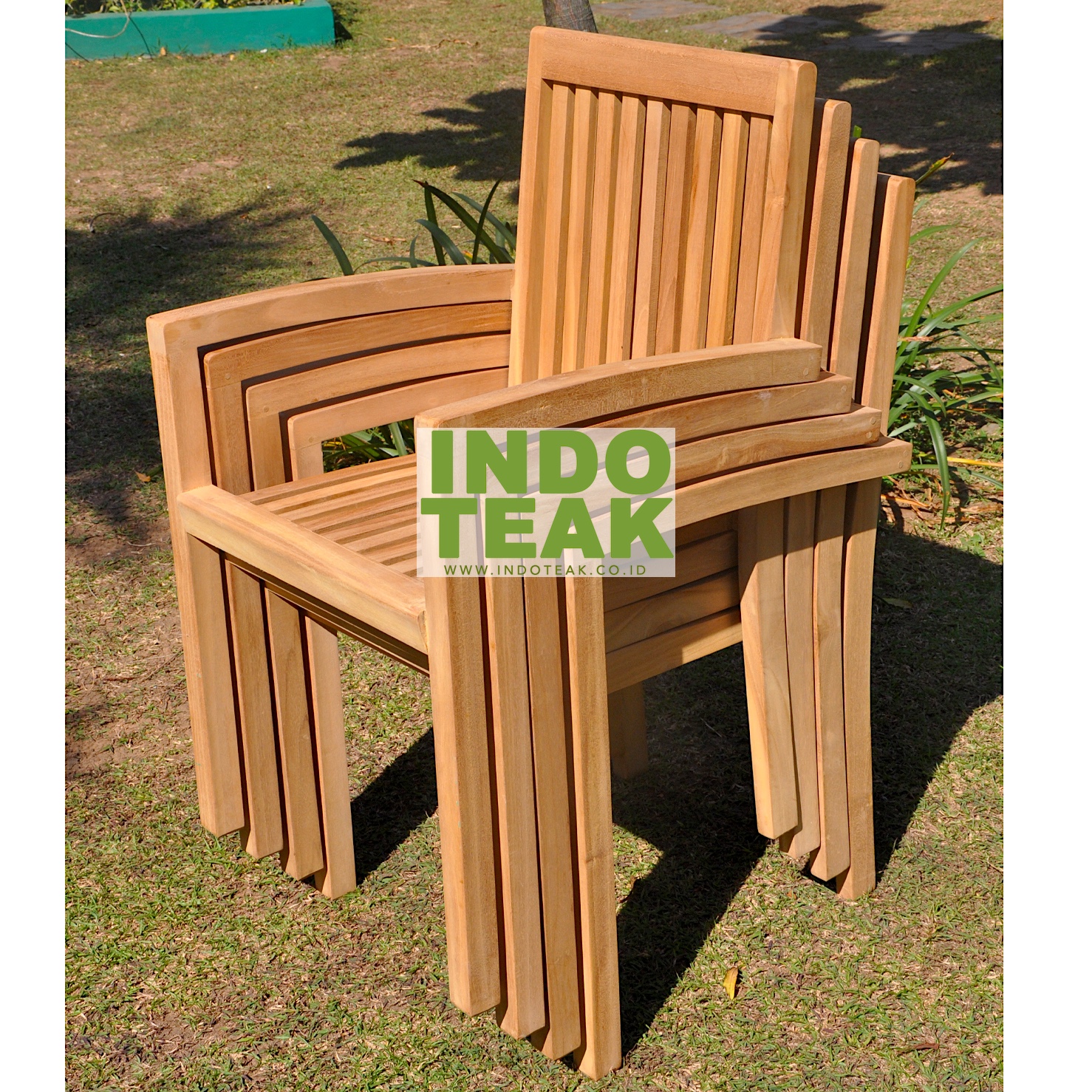 A stack of four premium solid teak stacking armchairs showcasing space-saving outdoor design and fine hand-sanded wood grain on green lawn.